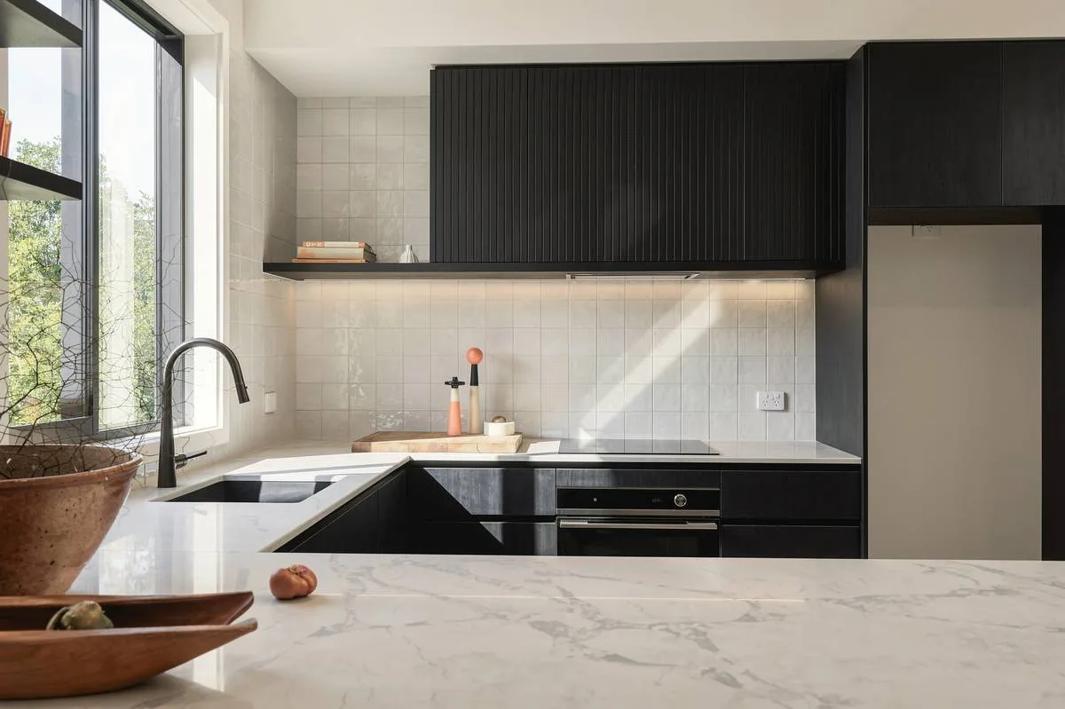 Blackened kitchen joinery against marble in morning light, editorial finish