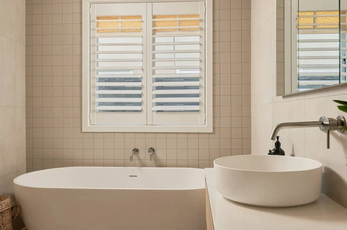 Freestanding bath under shuttered window light, editorial finish